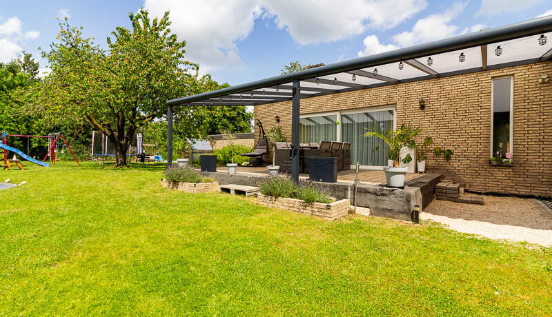 Weitläufiger Garten mit gepflegtem Rasen, Spielbereich und hochwertiger Terrassenüberdachung.